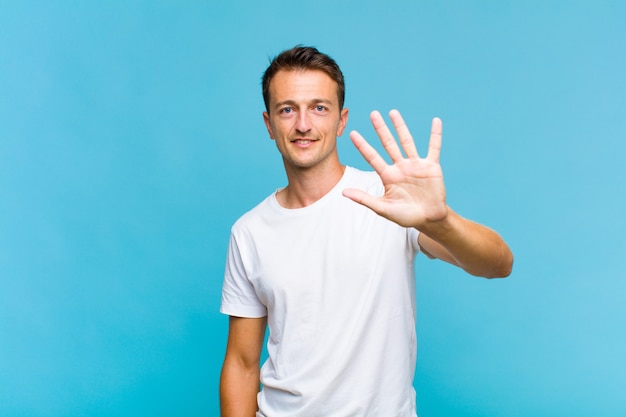 Young handsome man smiling and looking friendly, showing number five or fifth with hand forward, counting down