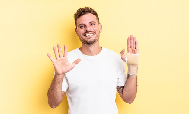 Young handsome man smiling and looking friendly, showing number five. hand bandage concept