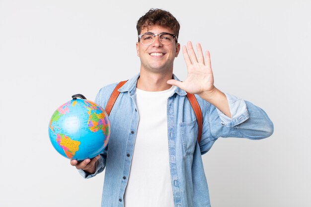 Foto giovane uomo bello che sorride e sembra amichevole, mostrando il numero cinque. studente con in mano una mappa del globo
