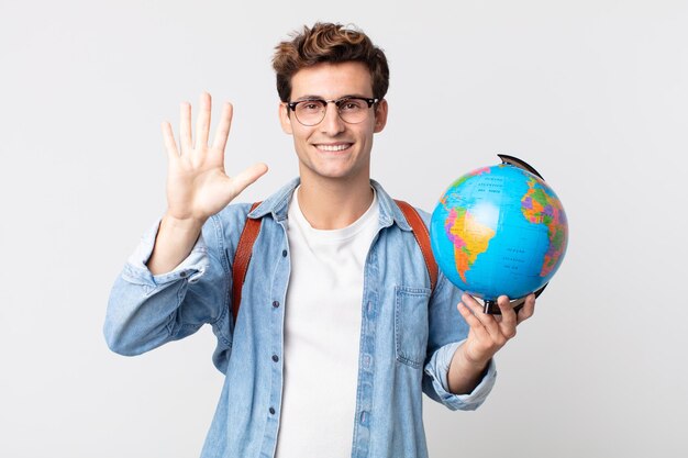 Foto giovane uomo bello che sorride e sembra amichevole, mostrando il numero cinque. studente con in mano una mappa del globo