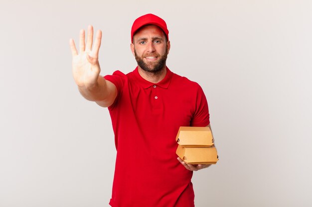 Young handsome man smiling and looking friendly, showing number four burger delivering concept