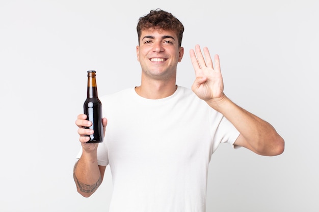 Young handsome man smiling and looking friendly, showing number four and holding a beer bottle