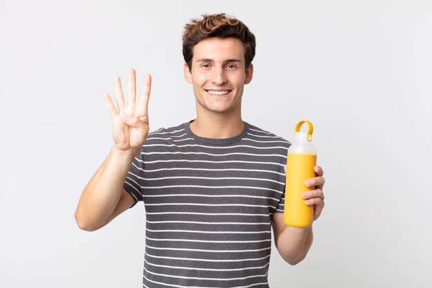 Giovane uomo bello che sorride e sembra amichevole, mostrando il numero quattro e tenendo un thermos di caffè