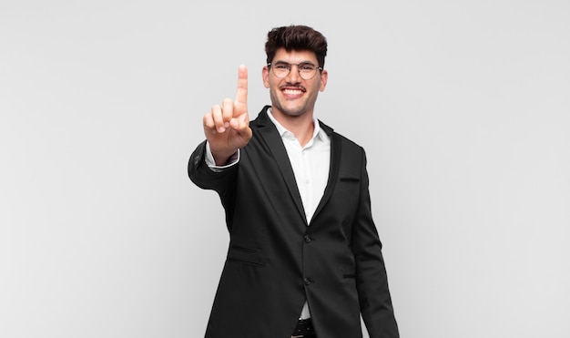 Young handsome man smiling and looking friendly, showing number one or first with hand forward, counting down