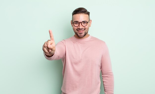 young handsome man smiling and looking friendly, showing number one or first with hand forward, counting down
