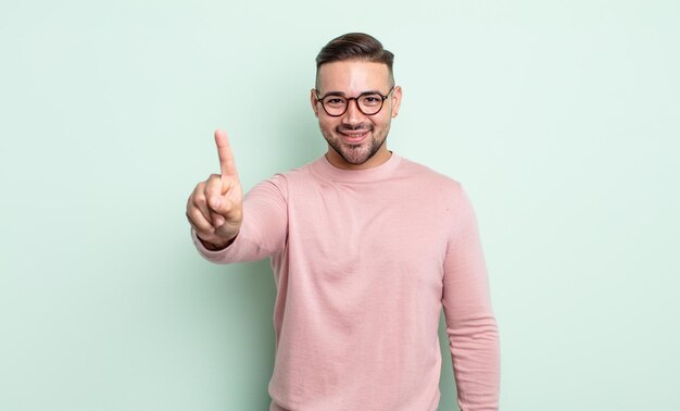 Young handsome man smiling and looking friendly, showing number one or first with hand forward, counting down