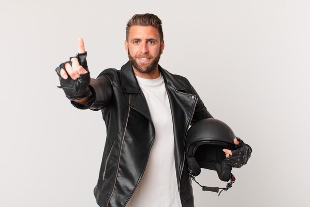 Young handsome man smiling and looking friendly, showing number one. motorbike helmet concept