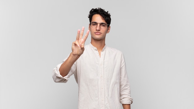 Young handsome man smiling and looking friendly, showing number three or third with hand forward, counting down