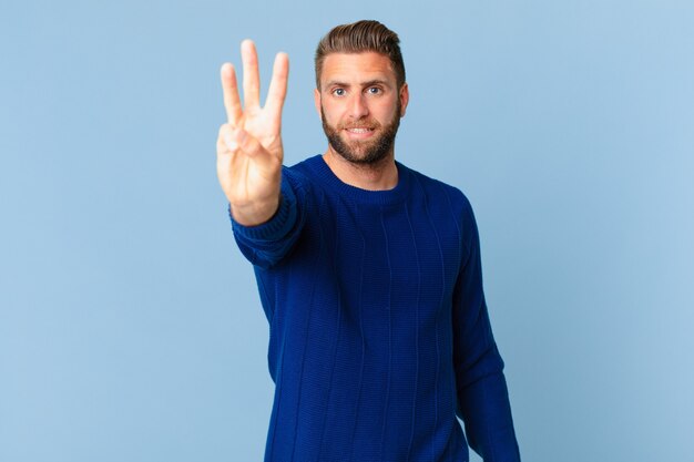 Young handsome man smiling and looking friendly, showing number three