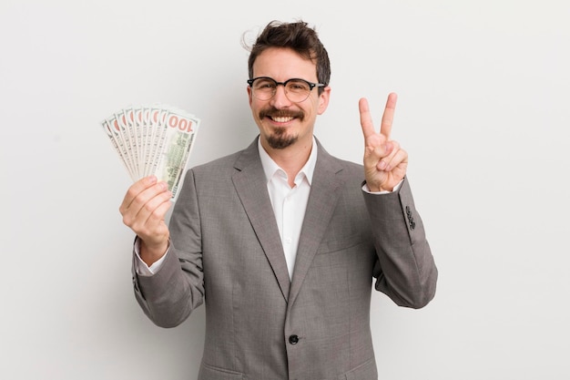 Young handsome man smiling and looking friendly showing number two businessman and banknotes