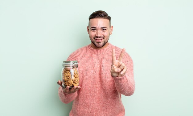 Young handsome man smiling and looking friendly, showing number two. cookies bottle concept