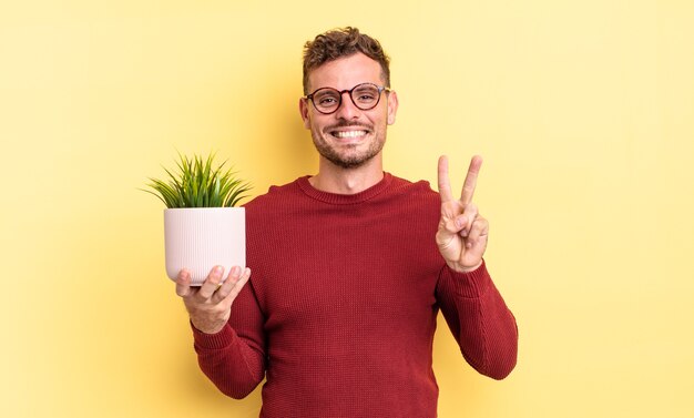 Young handsome man smiling and looking friendly, showing number two. decorative plant concept