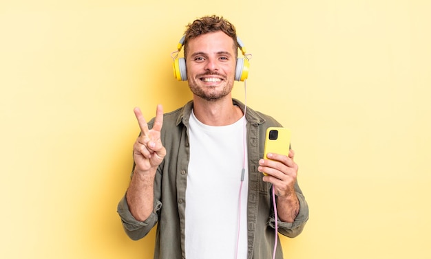 Young handsome man smiling and looking friendly, showing number two headphones and smartphone concept