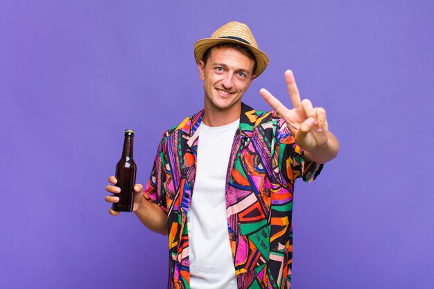 Young handsome man smiling and looking happy, carefree and positive, gesturing victory or peace with one hand