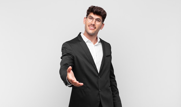 Young handsome man smiling, looking happy, confident and friendly, offering a handshake to close a deal, cooperating