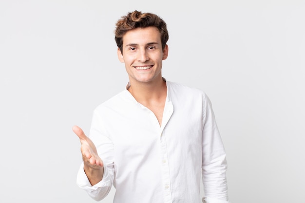 Young handsome man smiling, looking happy, confident and friendly, offering a handshake to close a deal, cooperating