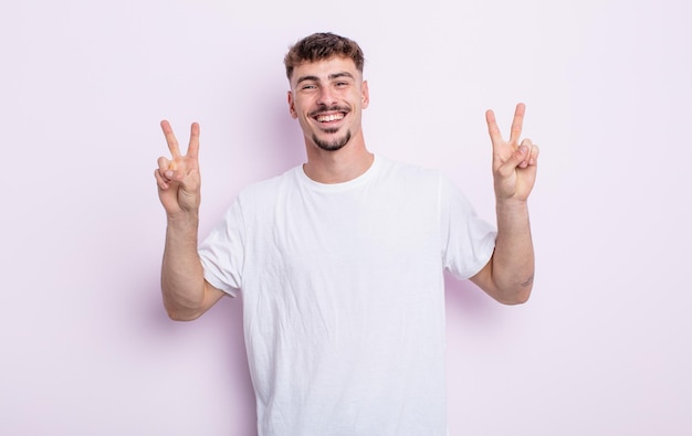 Young handsome man smiling and looking happy, friendly and satisfied, gesturing victory or peace with both hands