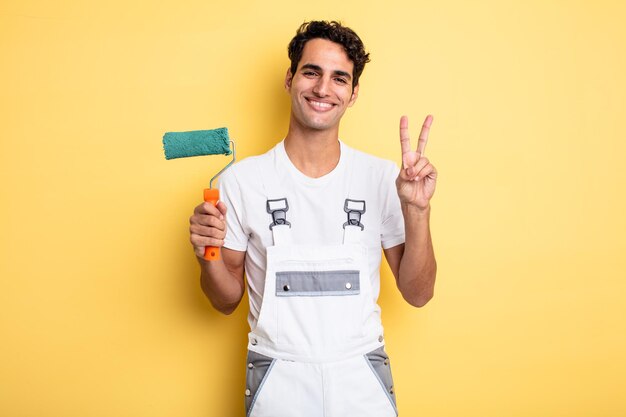 Young handsome man smiling and looking happy, gesturing victory or peace. painting home concept