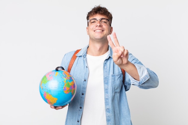 Giovane uomo bello che sorride e sembra felice, gesticolando vittoria o pace. studente con in mano una mappa del globo