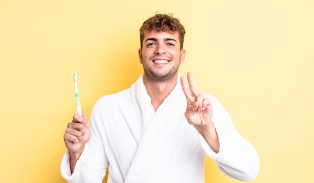 Young handsome man smiling and looking happy, gesturing victory or peace. toothbrush concept