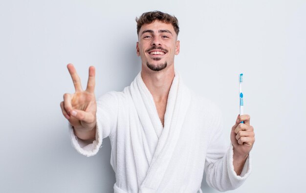 Young handsome man smiling and looking happy gesturing victory or peace toothbrush concept