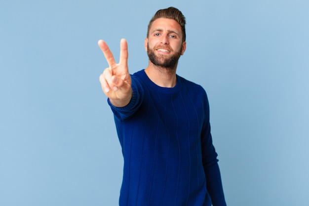 Young handsome man smiling and looking happy, gesturing victory or peace