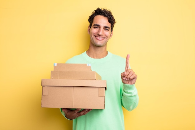 Young handsome man smiling proudly and confidently making number one. package boxes