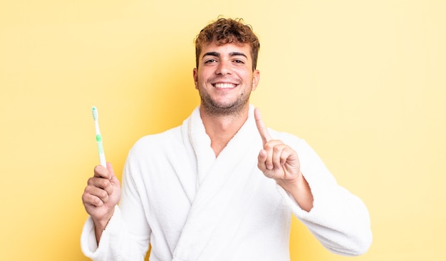 Young handsome man smiling proudly and confidently making number one. toothbrush concept