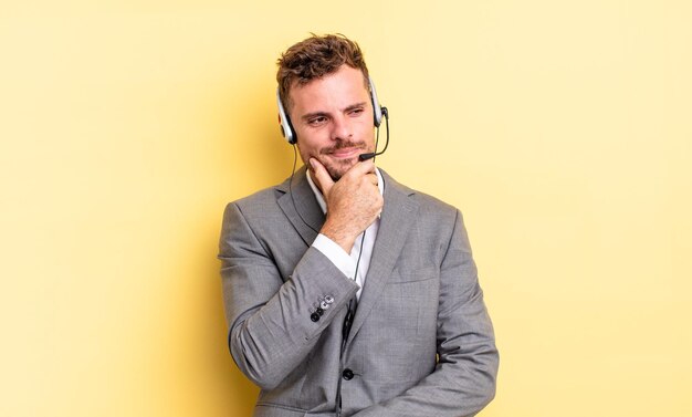 Young handsome man smiling with a happy, confident expression with hand on chin. telemarketer concetp