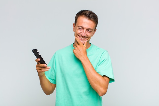 Young handsome man smiling with a happy, confident expression with hand on chin, wondering and looking to the side