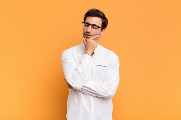 Young handsome man smiling with a happy, confident expression with hand on chin, wondering and looking to the side