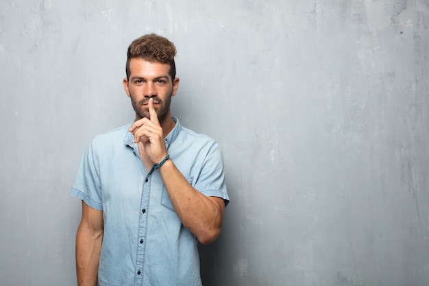 Young handsome man smiling, with index finger in front of mouth