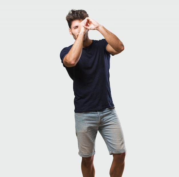 Young handsome man standing looking through a gap, hiding and squinting