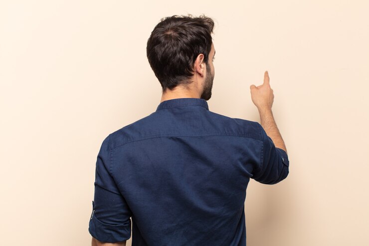 Photo young handsome man standing and pointing to object on copy space, rear view