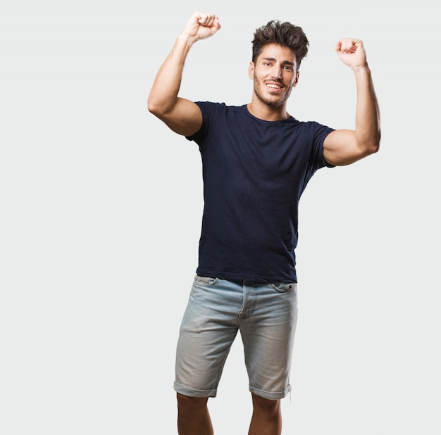 Giovane uomo bello in piedi molto felice ed emozionato, alzando le braccia, celebrando una vittoria o successo