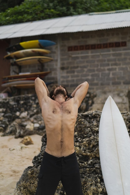 A young handsome man surfer on the ocean shore is doing a warm-up before surfing. exercises before sports, stretching before surfing.