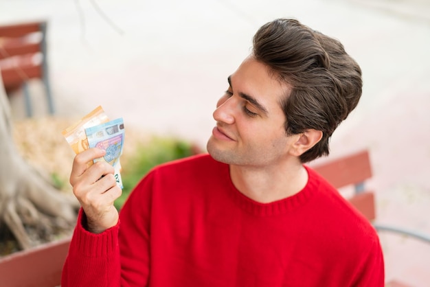 Young handsome man taking a lot of money with happy expression