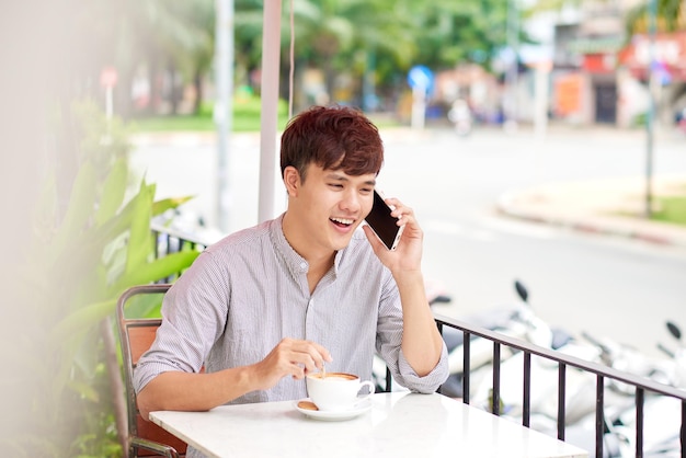 屋外のカフェに座って携帯電話で話している若いハンサムな男