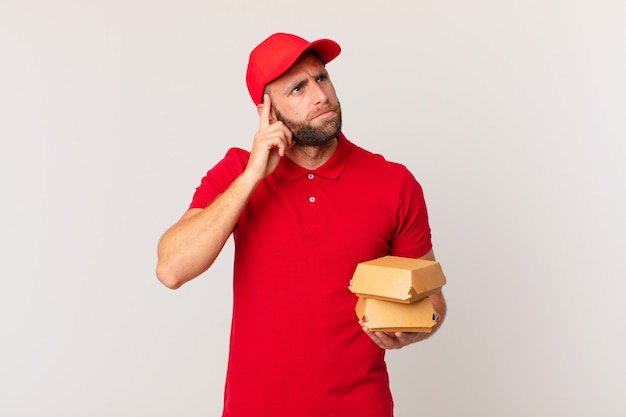 Young handsome man thinking, feeling doubtful and confused burger delivering concept