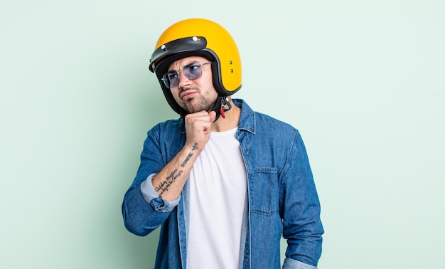 Young handsome man thinking feeling doubtful and confused motorbike helmet concept