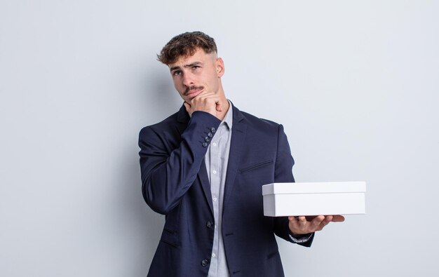 Young handsome man thinking, feeling doubtful and confused. white box package