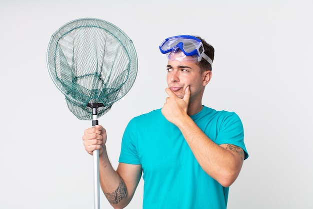 Young handsome man thinking, feeling doubtful and confused with goggles and fishing net