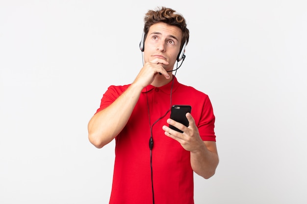 Young handsome man thinking, feeling doubtful and confused with a smartphone and headset