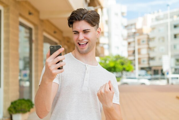 Young handsome man using mobile phone and doing victory gesture