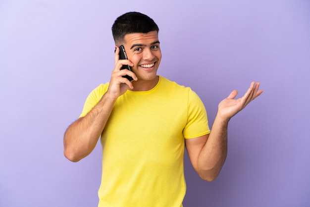 Young handsome man using mobile phone over isolated purple background extending hands to the side for inviting to come