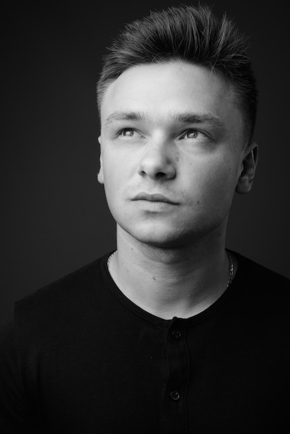 young handsome man wearing black shirt against gray wall. black and white