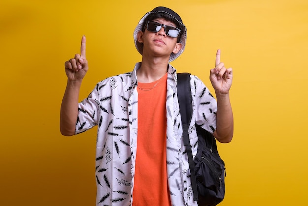 Young handsome man wearing casual beach clothes carrying backpack looking and pointing fingers abov