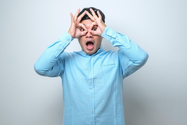 Young handsome man wearing casual shirt doing ok gesture like binoculars sticking tongue out eyes looking through fingers