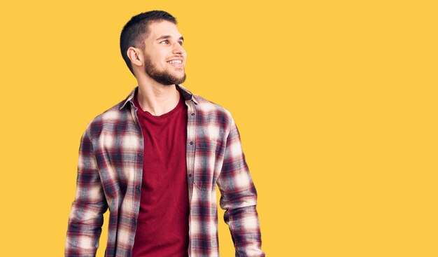 Young handsome man wearing casual shirt looking away to side with smile on face, natural expression. laughing confident.