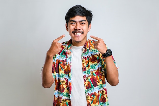 Foto giovane uomo bello che indossa una camicia casual in piedi su sfondo bianco isolato sorridente allegro mostrando e indicando con le dita i denti e la bocca. concetto di salute dentale.